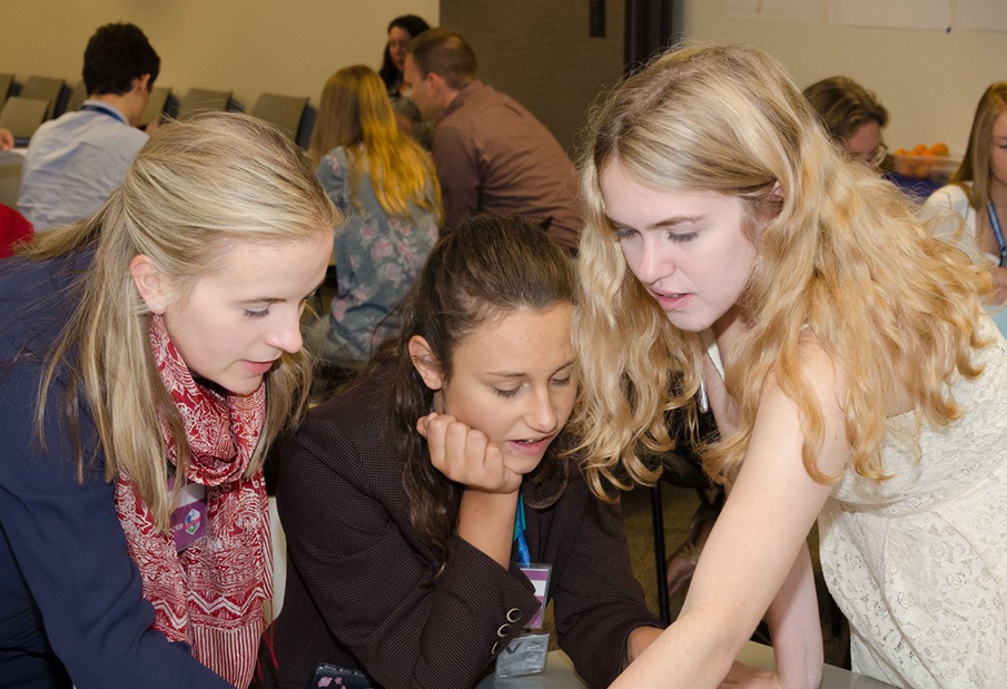 Three young women lean over a table working together on a project